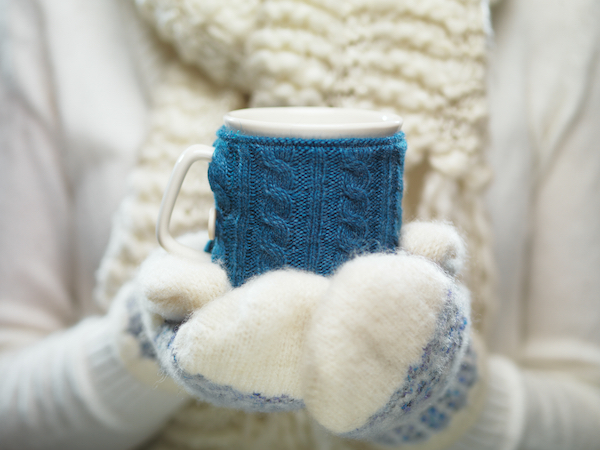 Female hands holding knitted winter mug close up. Woman hands in white and blue mittens holding a cozy knitted cup with hot cocoa, tea or coffee. Winter and Christmas time concept.